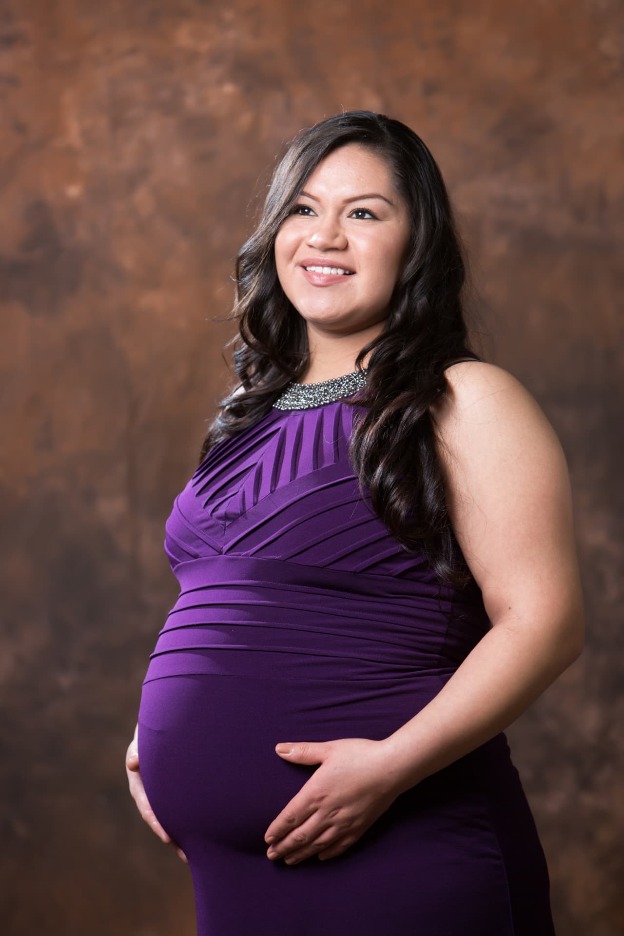 Expectant mother in an elegant purple gown posing in a studio portrait