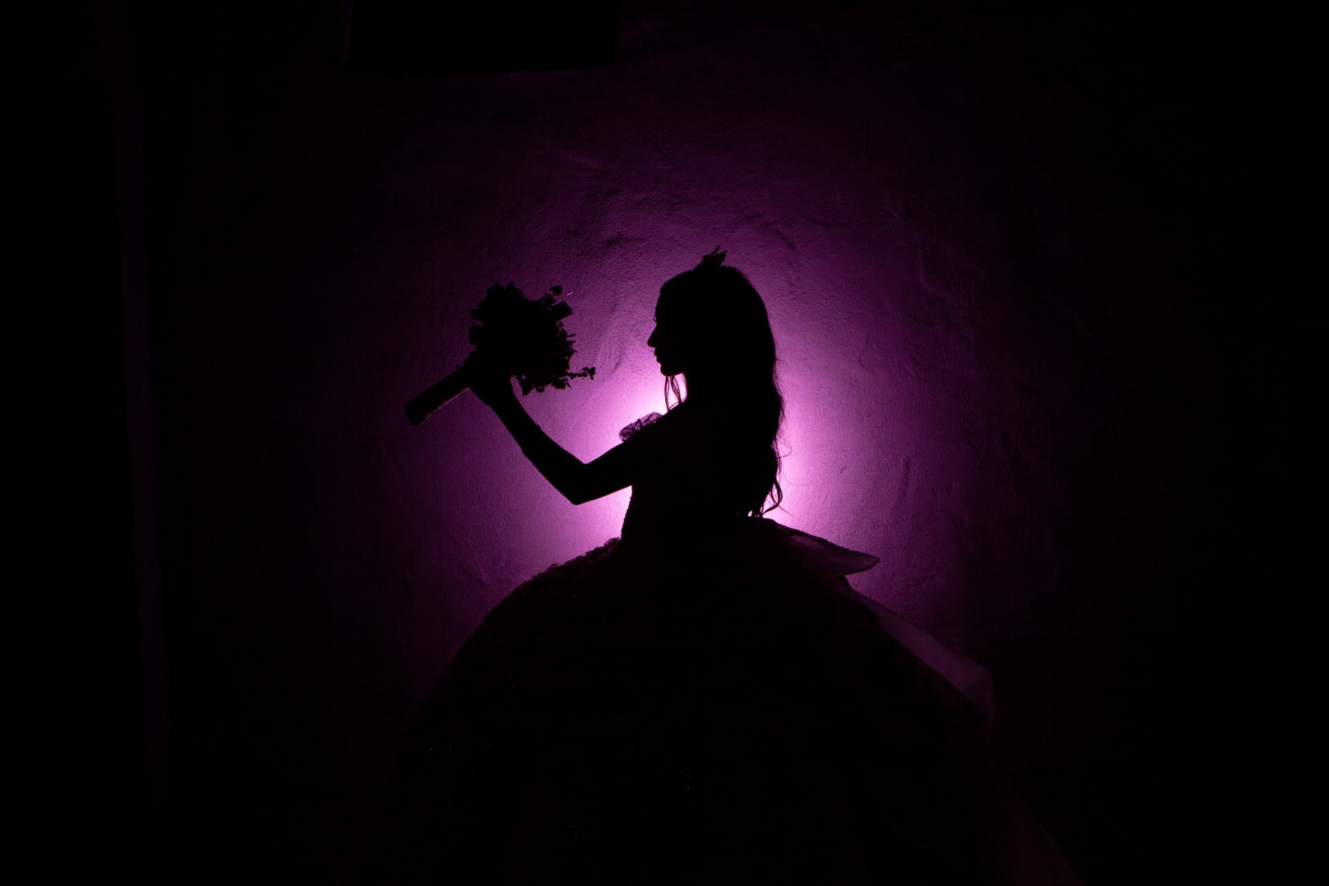 Bride silhouette holding her bouquet against a dramatic purple-lit wall